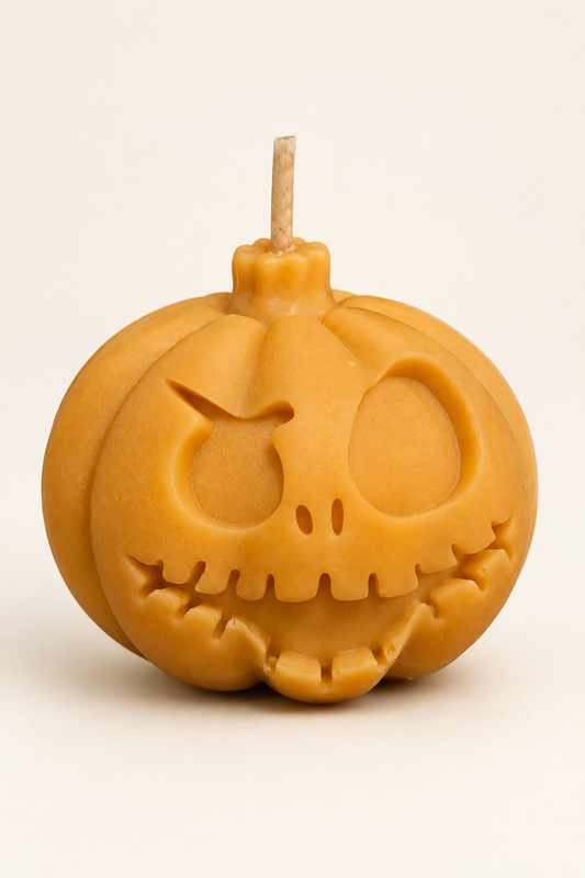 Bougie orange en forme de citrouille au visage grimaçant, avec une mèche, photographiée sur fond ivoire.