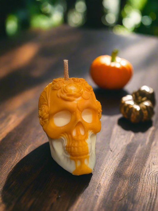 Bougie tête de mort orange et blanche ornée de roses, vue de face sur une table en bois avec une citrouille.
