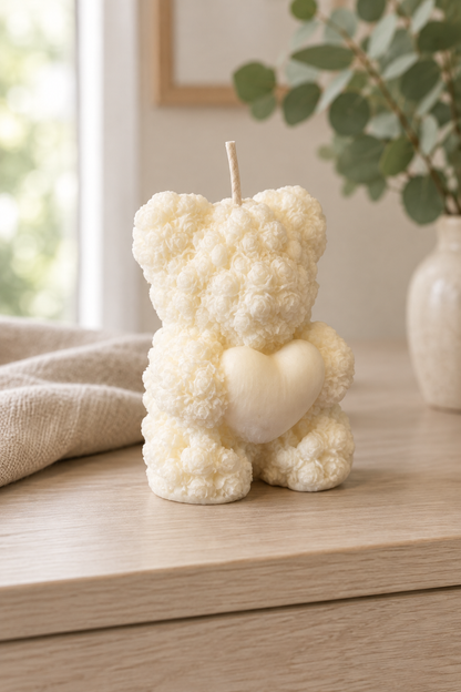 Bougie ivoire en forme d’ourson au relief de petites roses, tenant un cœur, avec une mèche, sur un meuble en bois clair.
