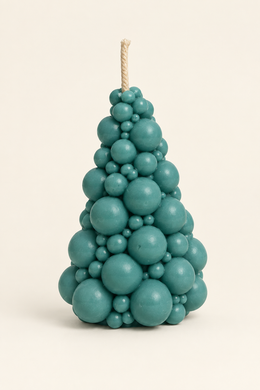 Bougie vert bleuté en forme de sapin composé de boules de différentes tailles, avec une mèche, photographiée sur fond ivoire.
