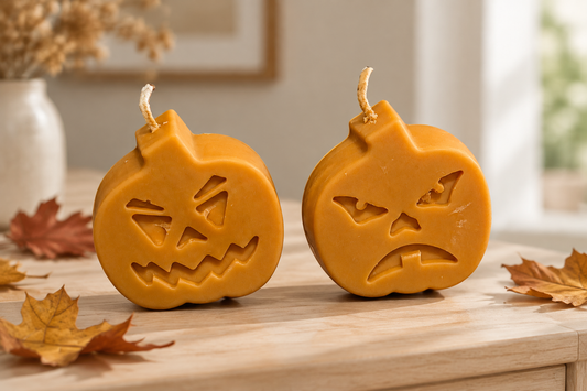 Deux bougies citrouilles plates orange, l’une souriante et l’autre mécontente, sur un meuble en bois avec des feuilles d’automne.
