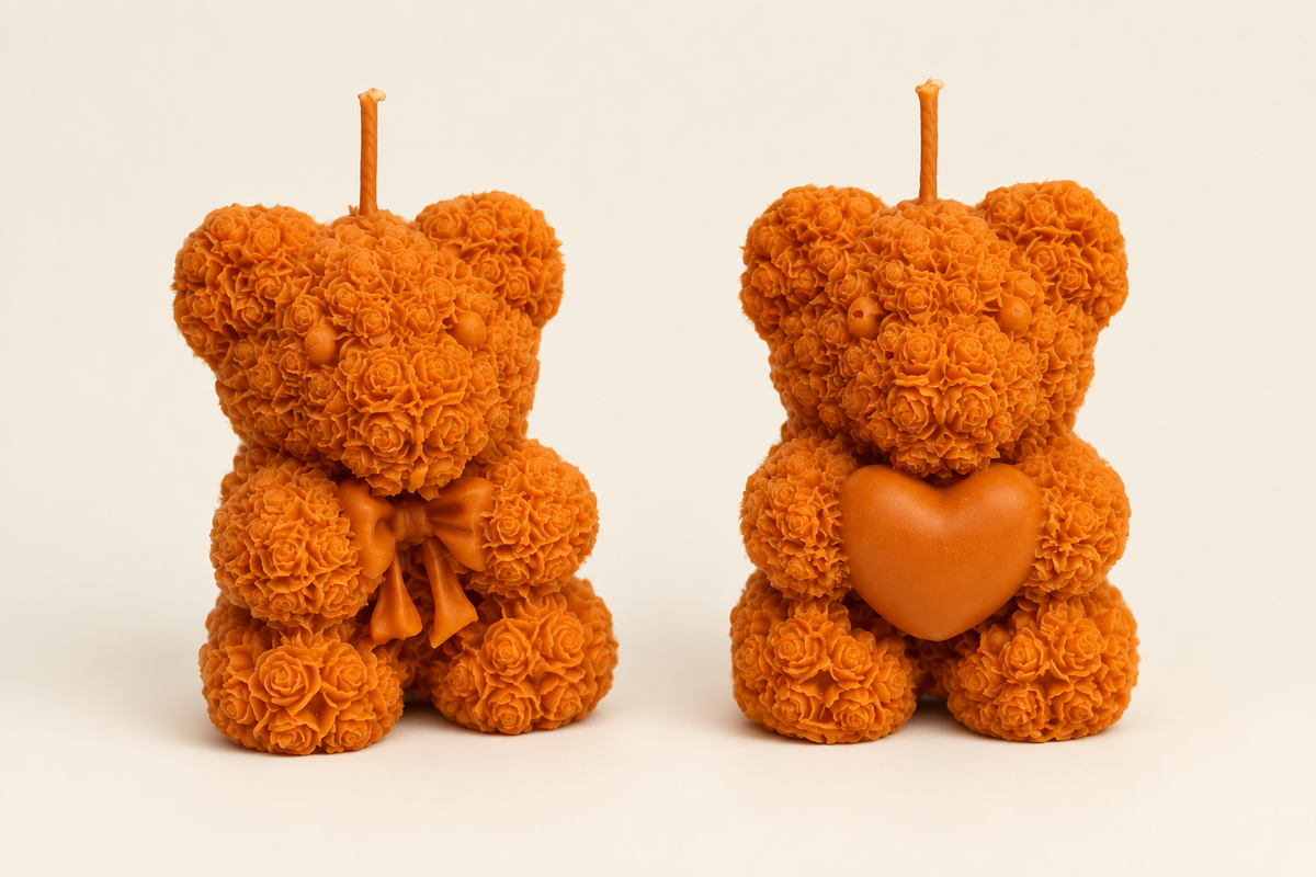 Deux bougies oursons orange au relief de roses, l’un avec un nœud et l’autre tenant un cœur, photographiées sur fond ivoire.
